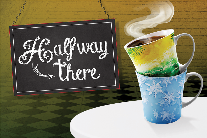A chalkboard sign reading “Halfway There” hangs on a green wall, next to two stacked coffee mugs—one with a winter theme and the other depicting a summer scene—on a white table, symbolizing the transition between seasons